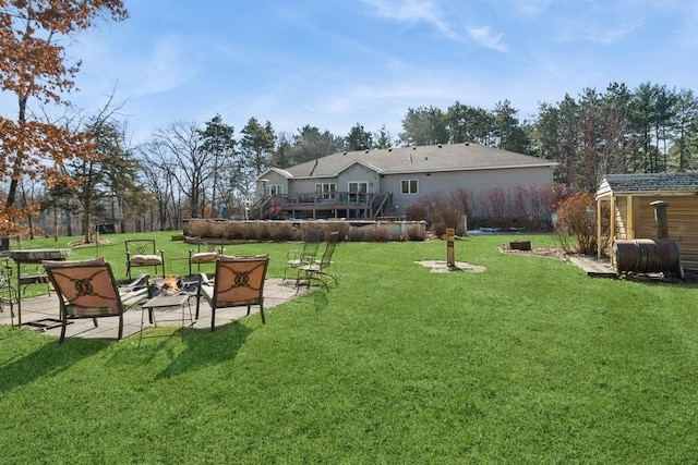 view of yard with a wooden deck, an outdoor structure, heating fuel, a fire pit, and a patio area