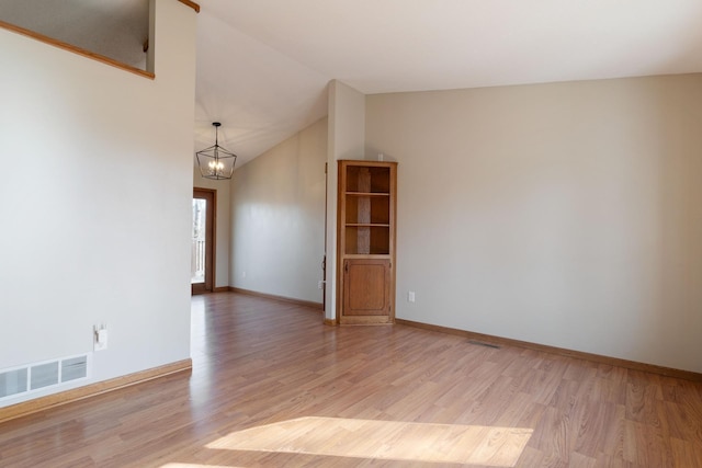 unfurnished room featuring baseboards, visible vents, lofted ceiling, light wood-style flooring, and a notable chandelier