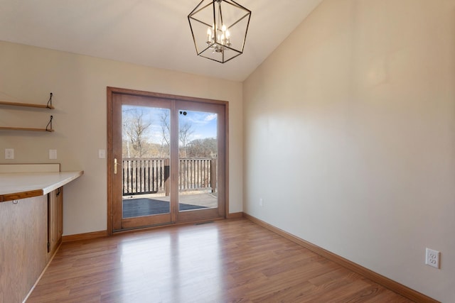 unfurnished dining area with a notable chandelier, baseboards, light wood-style floors, and lofted ceiling