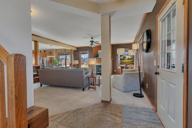 entryway featuring carpet floors, ceiling fan, a textured ceiling, a tiled fireplace, and crown molding