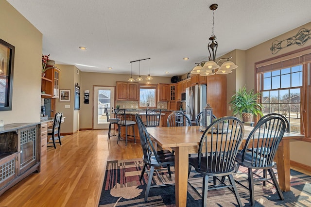 dining area featuring baseboards, light wood-type flooring, and a textured ceiling