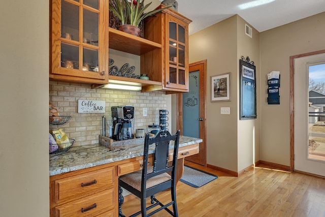 kitchen featuring visible vents, baseboards, light stone counters, built in desk, and light wood-style floors