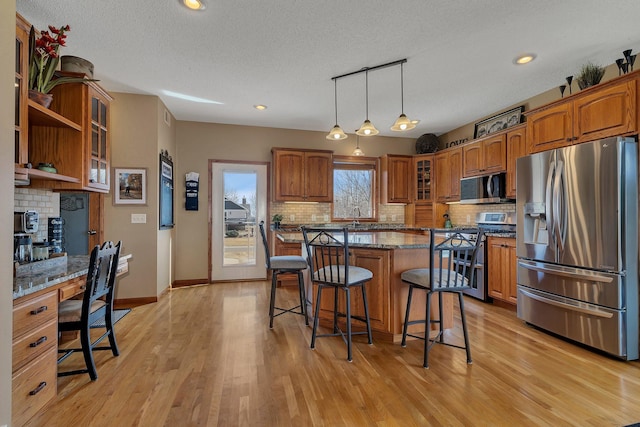 kitchen featuring glass insert cabinets, built in desk, a kitchen breakfast bar, brown cabinetry, and stainless steel appliances