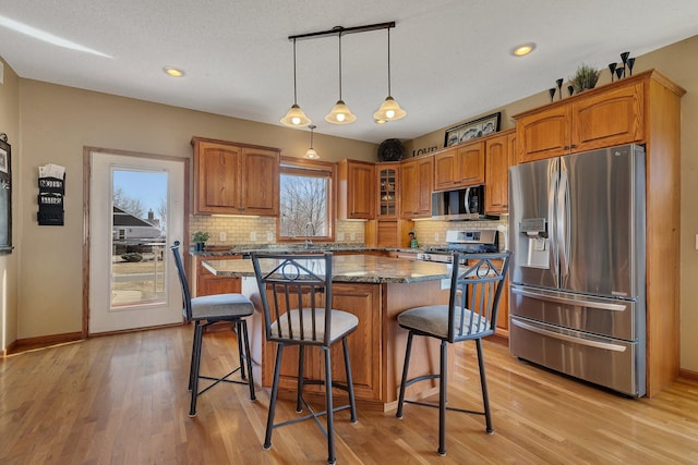 kitchen featuring a kitchen island, dark stone counters, a kitchen bar, brown cabinetry, and stainless steel appliances