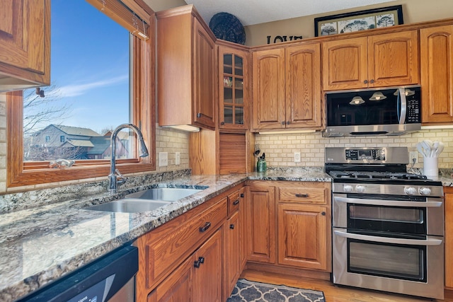 kitchen with a sink, light stone countertops, appliances with stainless steel finishes, and brown cabinets