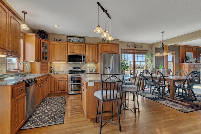 kitchen with a sink, a kitchen breakfast bar, light wood-style floors, appliances with stainless steel finishes, and glass insert cabinets