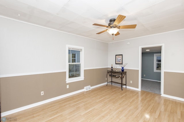 unfurnished room featuring baseboards, visible vents, a ceiling fan, ornamental molding, and wood finished floors