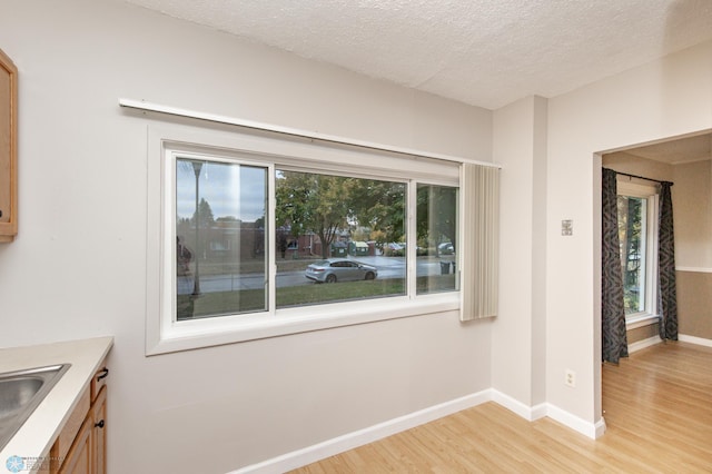 interior space with a textured ceiling, light wood finished floors, and baseboards