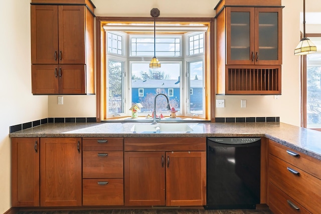 kitchen with black dishwasher, hanging light fixtures, brown cabinetry, a sink, and dark stone counters