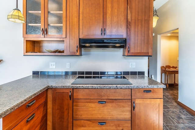 kitchen featuring black electric stovetop, hanging light fixtures, brown cabinetry, glass insert cabinets, and under cabinet range hood