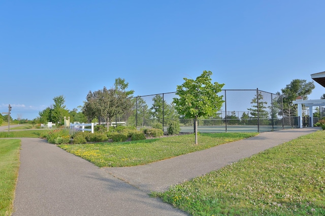 view of home's community featuring a tennis court, a yard, and fence