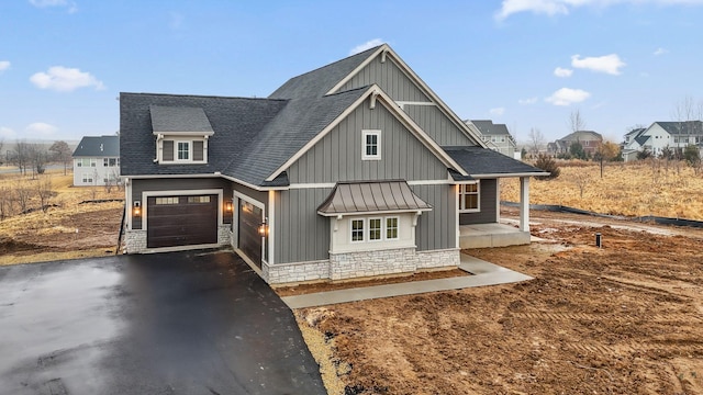 view of front of home with stone siding, a shingled roof, metal roof, and aphalt driveway