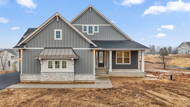 view of front facade with metal roof, a porch, stone siding, roof with shingles, and a standing seam roof