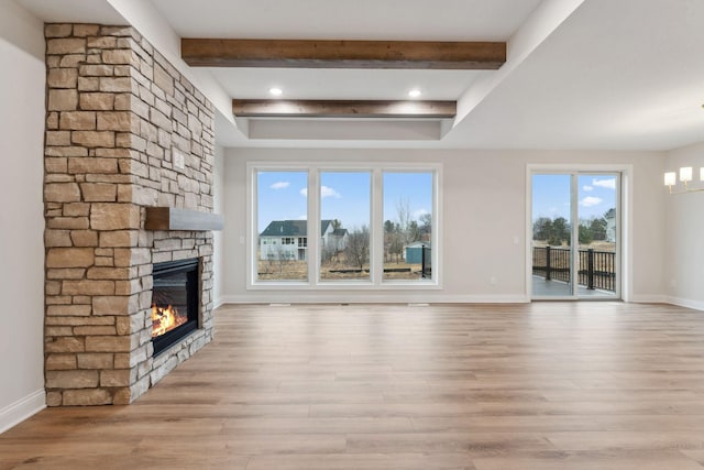 unfurnished living room with baseboards, a stone fireplace, beam ceiling, and light wood-style floors