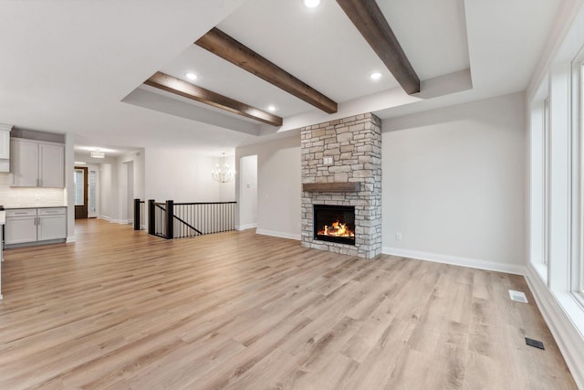 unfurnished living room featuring baseboards, visible vents, light wood-style floors, a fireplace, and beam ceiling