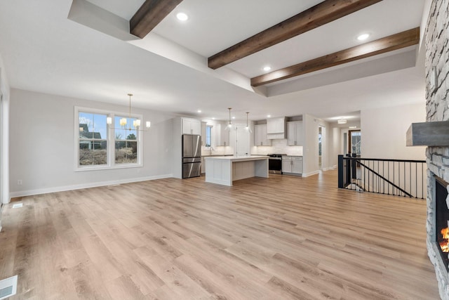 unfurnished living room featuring light wood-style floors, a fireplace, a chandelier, and beamed ceiling