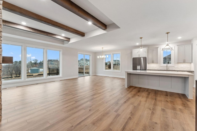 unfurnished living room featuring a notable chandelier, recessed lighting, light wood-style flooring, beamed ceiling, and baseboards