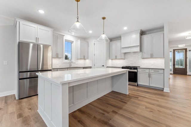 kitchen featuring light wood finished floors, appliances with stainless steel finishes, a center island, light countertops, and a sink