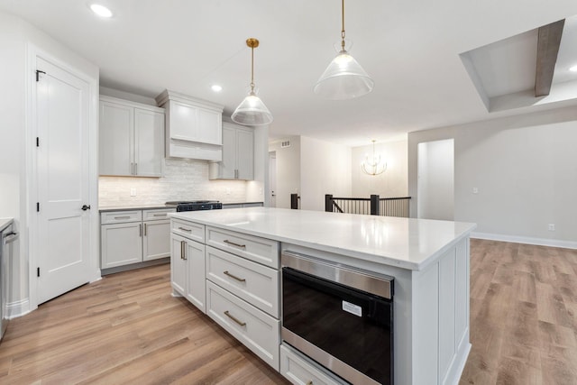 kitchen with hanging light fixtures, tasteful backsplash, light wood-type flooring, and built in microwave