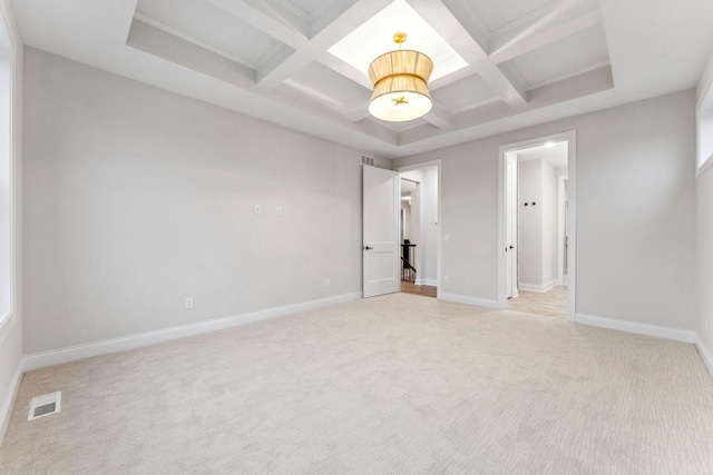 empty room featuring coffered ceiling, light colored carpet, visible vents, and baseboards