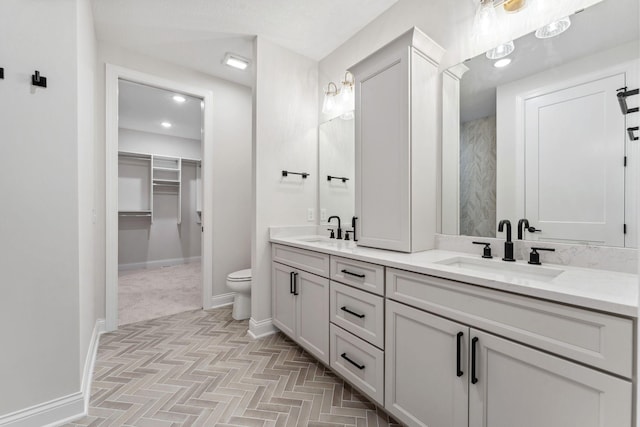 bathroom with double vanity, a sink, toilet, and baseboards