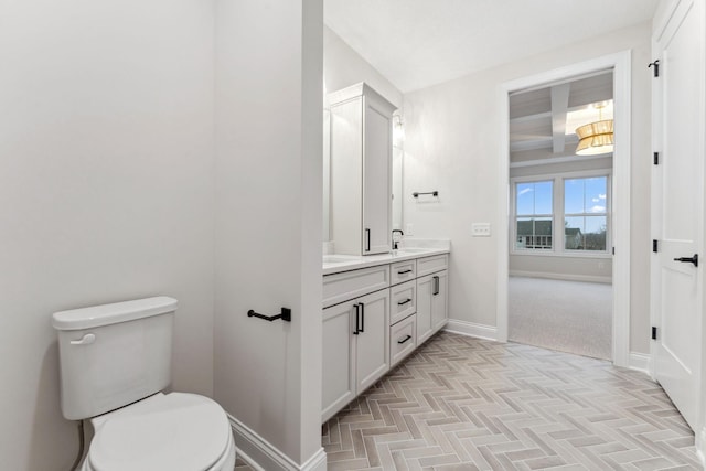 bathroom featuring toilet, a sink, baseboards, beam ceiling, and double vanity