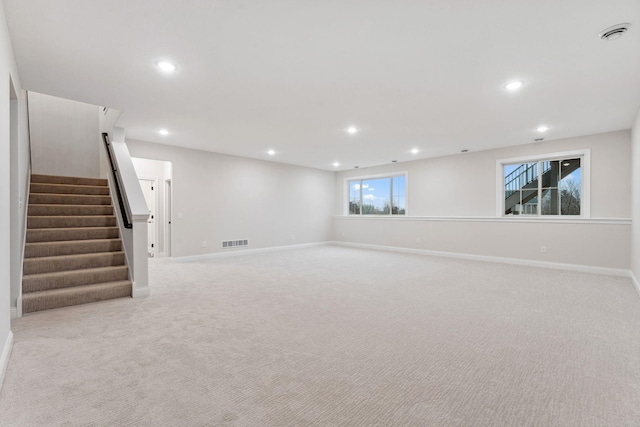 basement with light carpet, visible vents, stairway, and baseboards