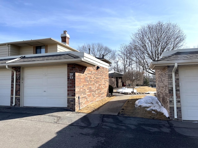 view of home's exterior with a garage, brick siding, a chimney, and a shingled roof