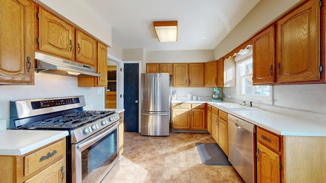 kitchen featuring brown cabinetry, stainless steel appliances, light countertops, under cabinet range hood, and a sink