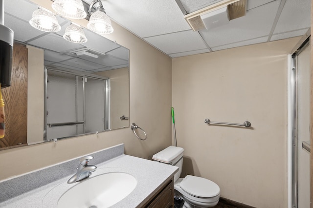 full bathroom with a shower with shower door, a drop ceiling, toilet, and vanity