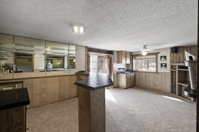 kitchen with a textured ceiling, dark countertops, wooden walls, and light carpet