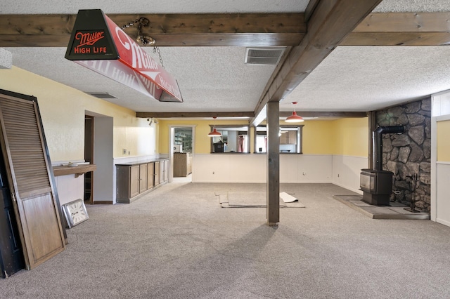 finished basement featuring a wood stove, carpet flooring, visible vents, and a textured ceiling