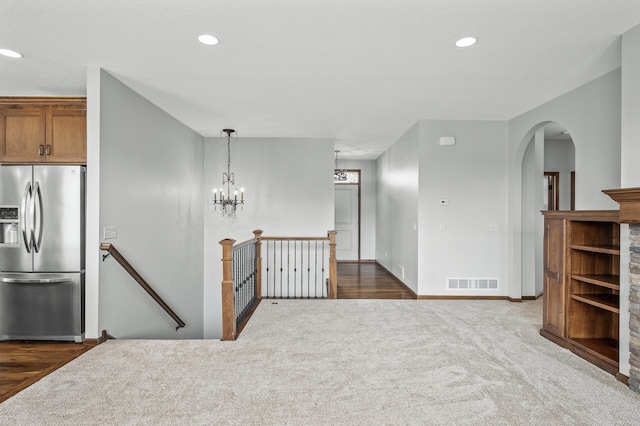 interior space with dark colored carpet, stainless steel fridge, visible vents, brown cabinetry, and arched walkways