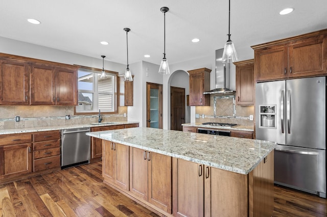 kitchen with tasteful backsplash, wall chimney exhaust hood, a sink, appliances with stainless steel finishes, and a kitchen island