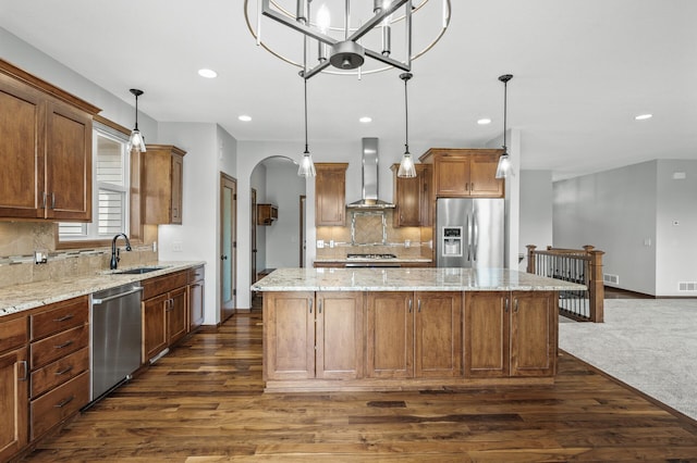 kitchen with appliances with stainless steel finishes, wall chimney range hood, a kitchen island, dark wood finished floors, and a sink