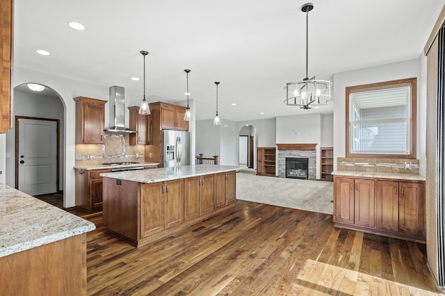 kitchen featuring wall chimney range hood, arched walkways, stainless steel appliances, and dark wood-type flooring