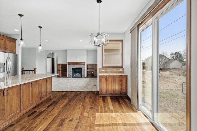 kitchen featuring stainless steel fridge with ice dispenser, brown cabinetry, light stone countertops, and dark wood-type flooring