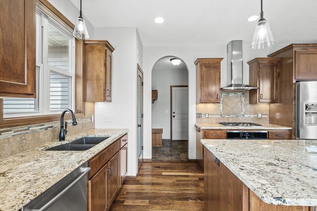 kitchen with dark wood-style flooring, wall chimney range hood, appliances with stainless steel finishes, arched walkways, and a sink