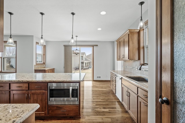 kitchen featuring dishwashing machine, wood finished floors, stainless steel microwave, a sink, and decorative light fixtures