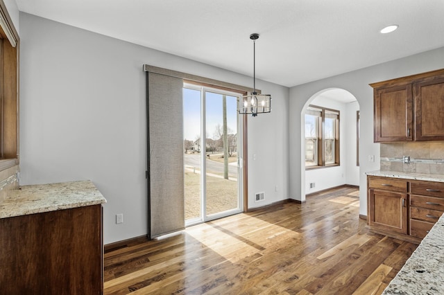unfurnished dining area featuring arched walkways, a notable chandelier, visible vents, and wood finished floors