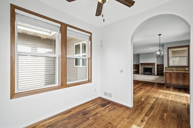 unfurnished room with visible vents, ceiling fan, arched walkways, and wood finished floors