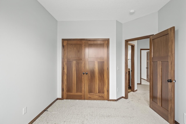 unfurnished bedroom with a closet, light colored carpet, and baseboards
