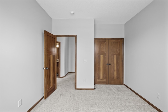 unfurnished bedroom with a closet, light colored carpet, and baseboards