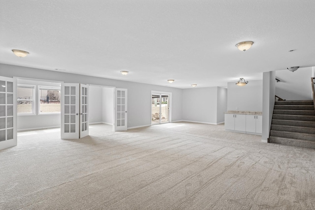 unfurnished living room with baseboards, light carpet, stairway, french doors, and a textured ceiling