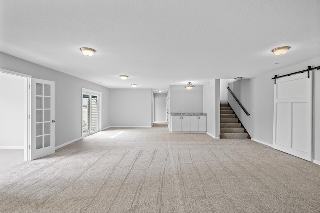 below grade area featuring a textured ceiling, stairway, a barn door, light carpet, and baseboards