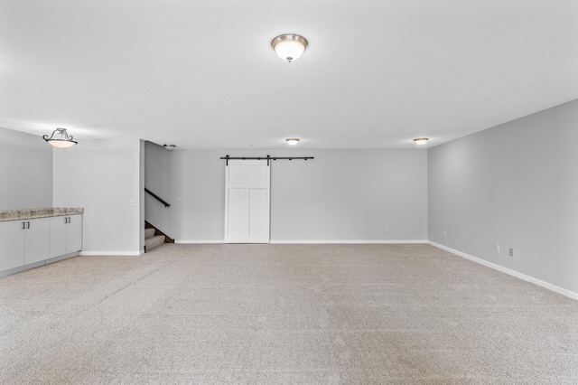 unfurnished room with baseboards, stairway, a barn door, and light carpet