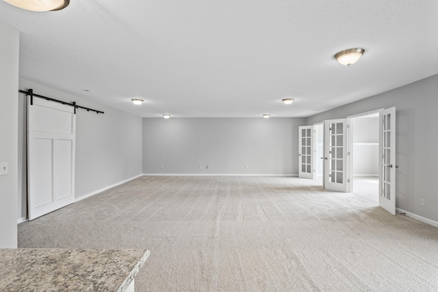 below grade area featuring a barn door, french doors, baseboards, and light colored carpet