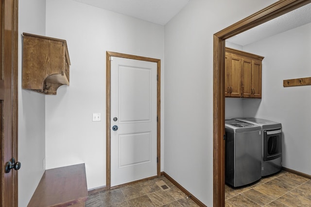 clothes washing area featuring stone finish floor, washing machine and clothes dryer, baseboards, and cabinet space