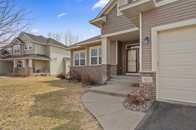 entrance to property with a garage, brick siding, and a lawn