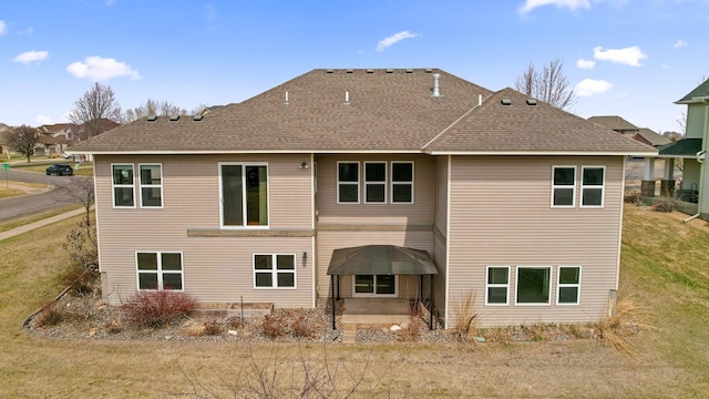 rear view of property featuring a shingled roof and a lawn
